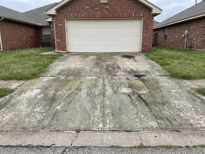 Concrete driveway covered in green algae film, dark mildew and oil staining before cleaning