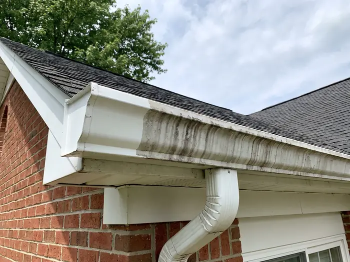White aluminium gutter with dark tiger-stripe staining on one section and cleaned bright white on another
