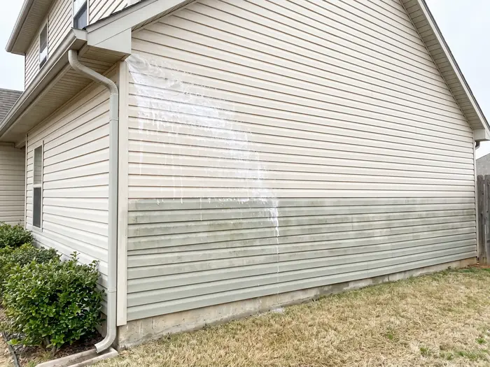 Vinyl house siding part-way through a soft wash, clean above and mildewed below
